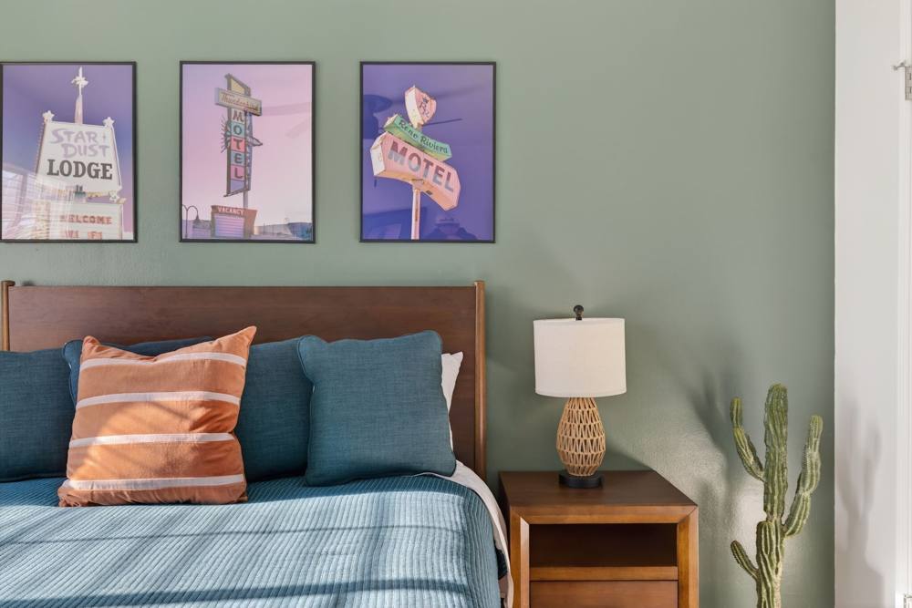 Bedroom with a sage green accent wall, three framed vintage Reno motel sign prints, teal bedding and an apricot striped pillow